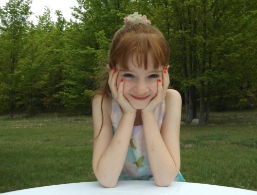 kislány piros körömmel, hát mögött erdővel