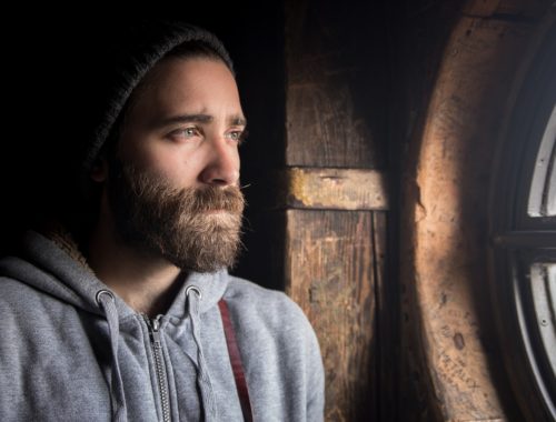 szakállas férfi néz ki egy ablakon