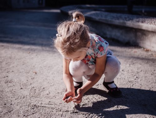 egy kislány guggol és homok van a kezében