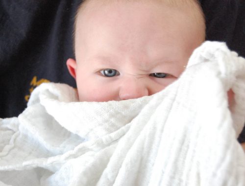 kisbaba grimaszol és elbújik a takarója mögé