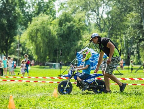 kisfiú motorral megy egy akadálypályán egy férfi segít neki