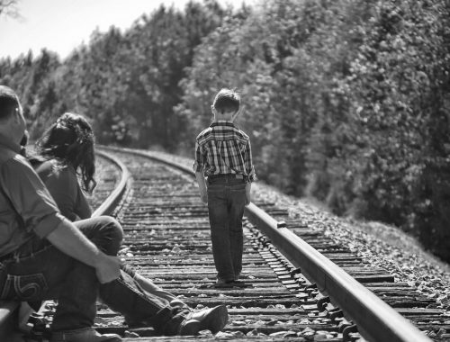 kisfiú sétál a vonatsíneken, a szülei nézik