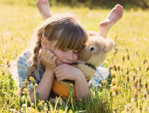 Kislány a réten egy játékmackóval.